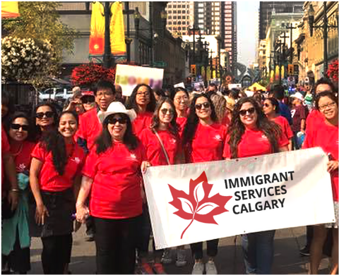 A group of Immigrant Services Calgary staff and volunteers smile and cheer on a sunny day in downtown Calgary